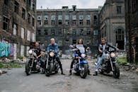 Notre histoire -Equipe au complet de Equipmoto Four bikers in front of a graffiti-covered abandoned building, capturing urban lifestyle
